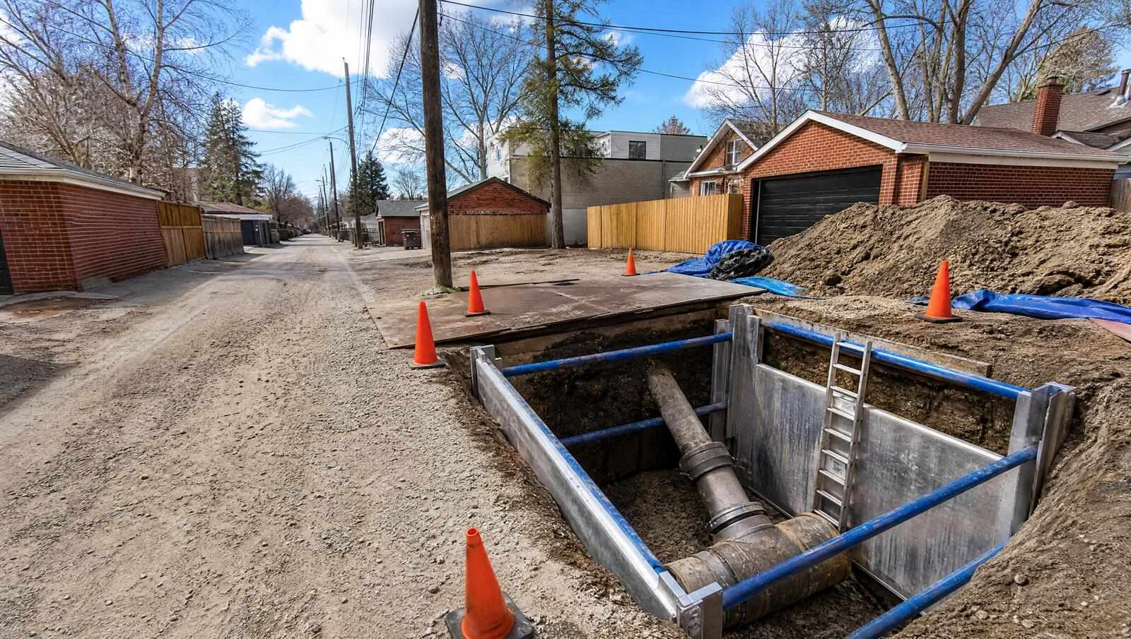 A deep shored excavation in a Denver alley exposing the point where a private sewer lateral joins the larger public sewer main at a wye tap.